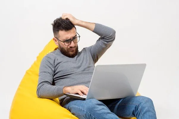 Um homem sentado com um notebook e uma expressão preocupada.